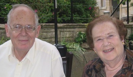 An older couple sat outside near plants, smiling