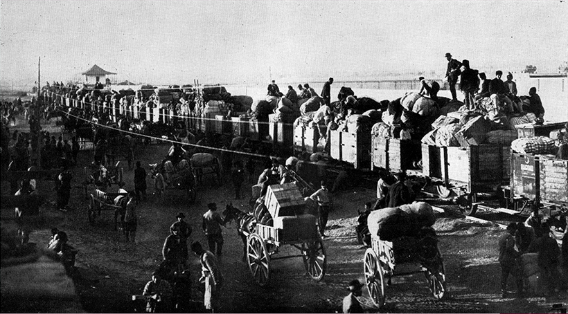 Black and white photograph depicting people packing their belongings onto a train