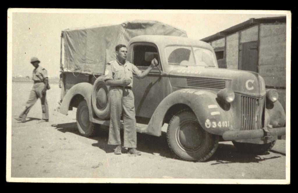 A man photographed in front of an army truck, 1940s